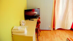 A room with a bed, a TV, a desk, and a chair.
