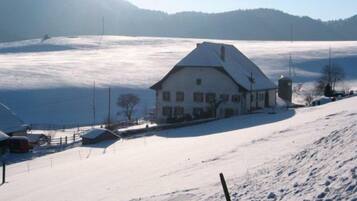 A snow-covered landscape with a white building that appears to be a hotel, surrounded by a snowy field and a mountain in the background.