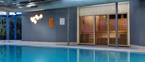 Een zwembad met een modern architectonisch ontwerp, inclusief een glazen overkapping en een houten sauna-gedeelte.