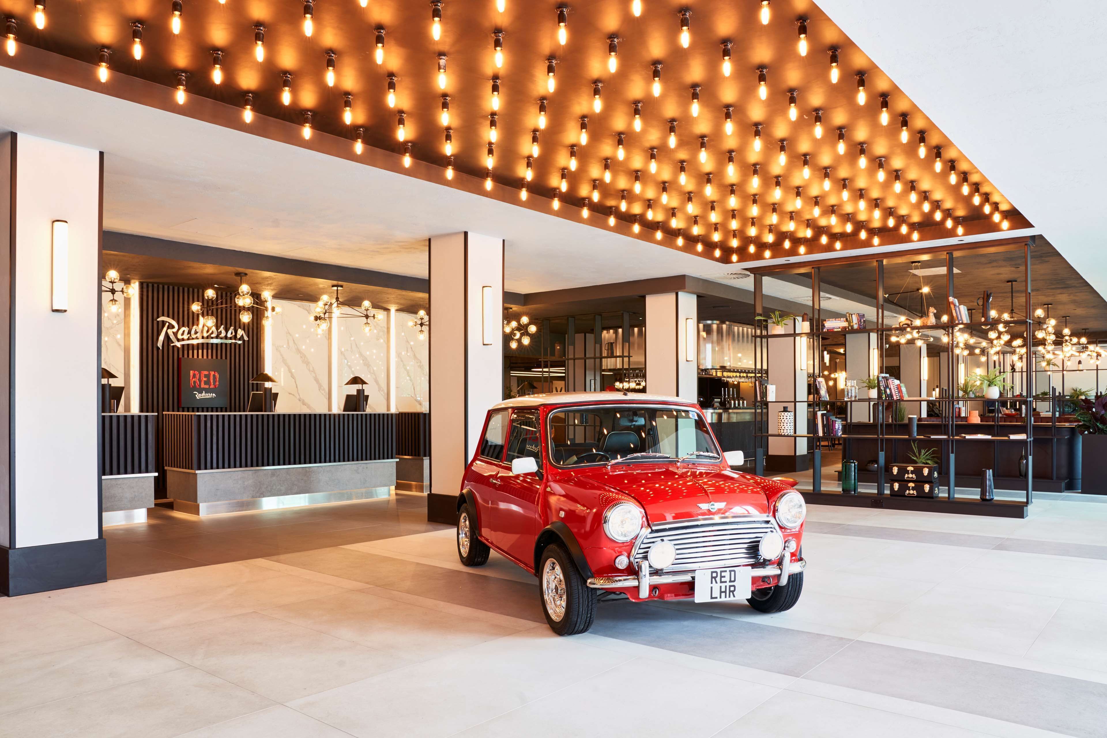 Ein roter Mini Cooper steht in der modernen Hotelhalle mit stilvollem Deckenstil und einem Empfangsbereich.