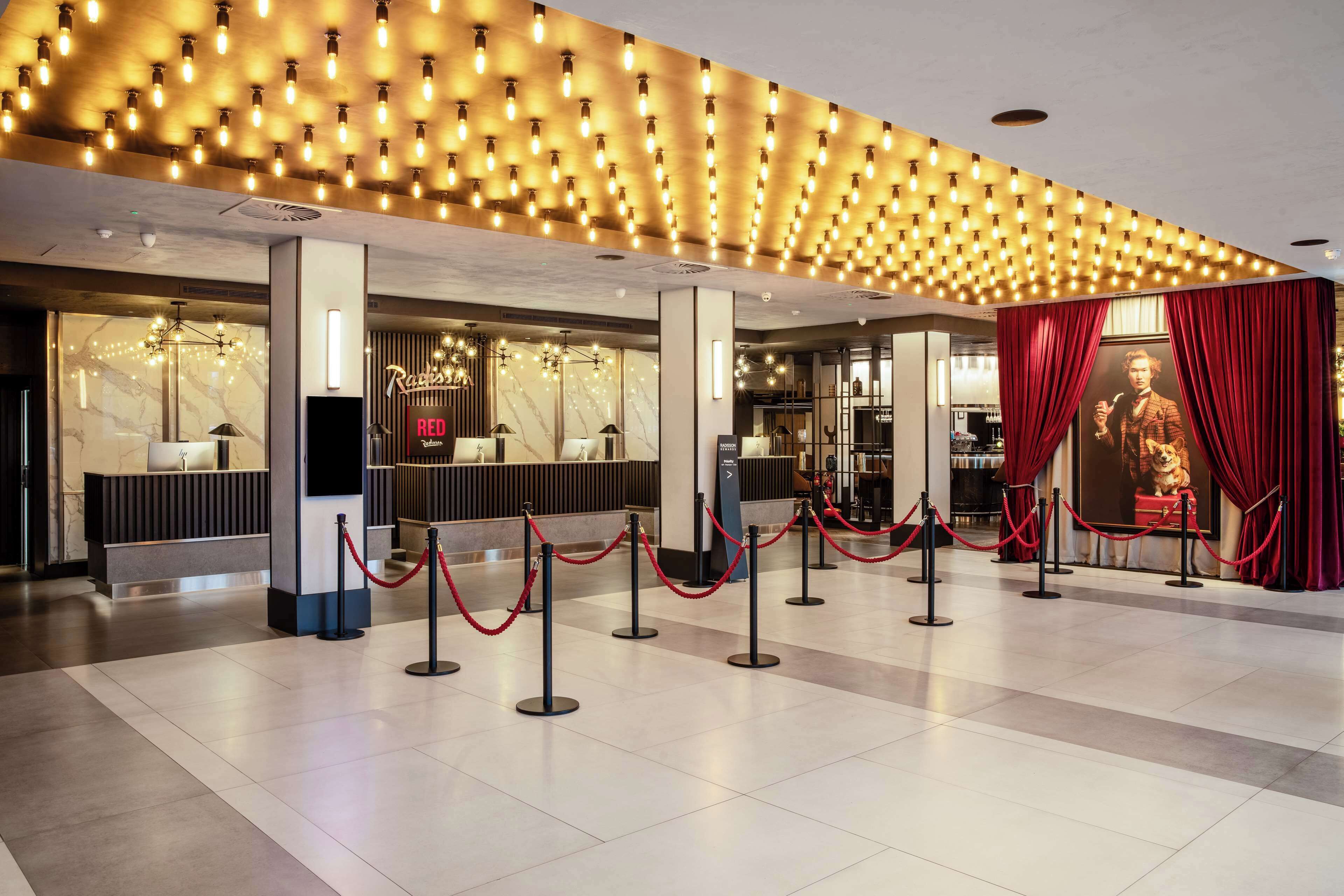 A hotel lobby with a reception desk, a red curtain backdrop, and a patterned ceiling.