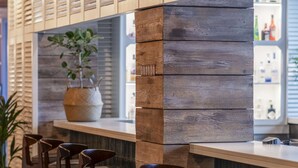 A bar area with wooden slats, a potted plant, and bar stools.