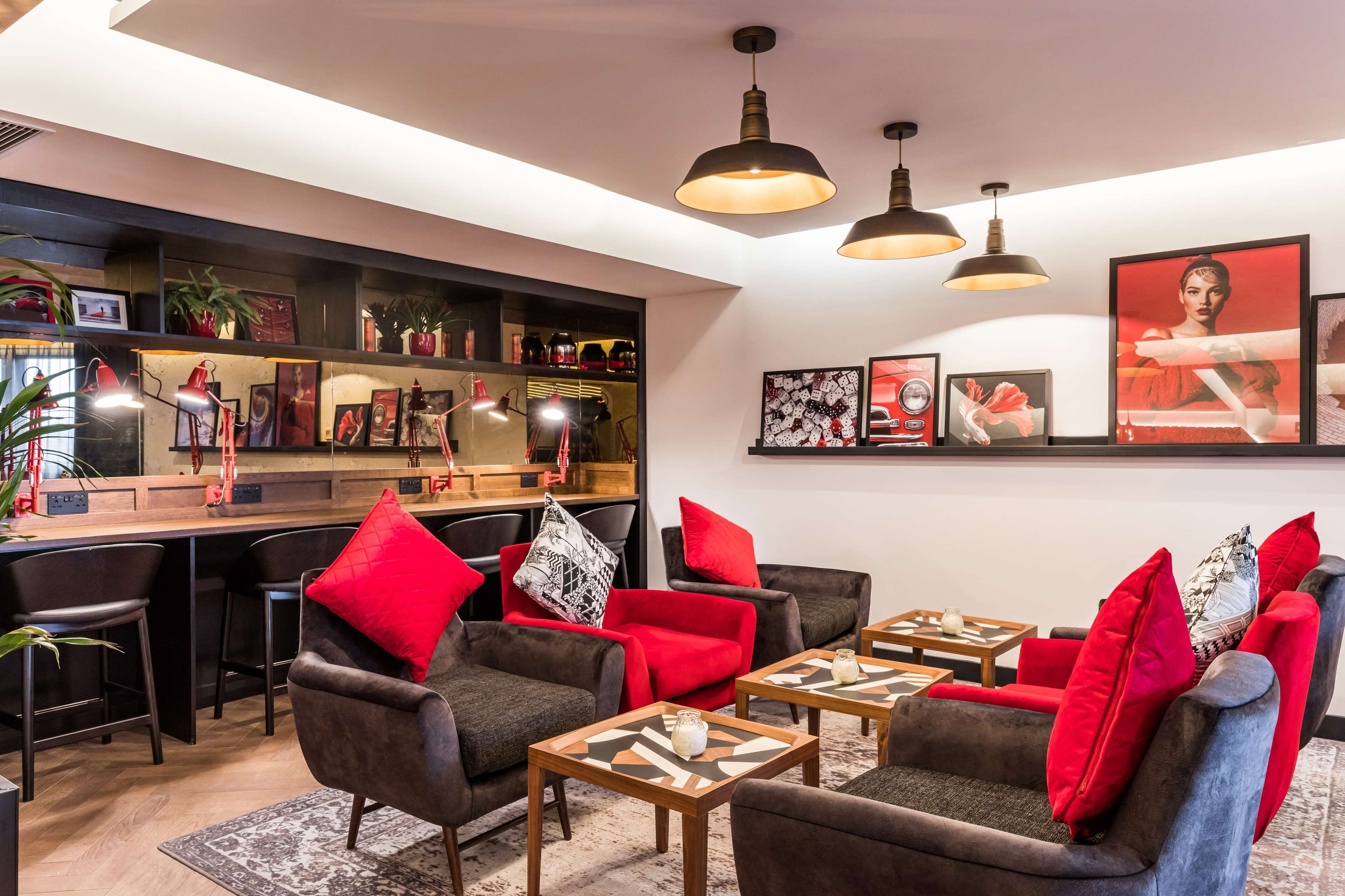 A modern living area with a bar, seating with red cushions, and artwork on the walls.