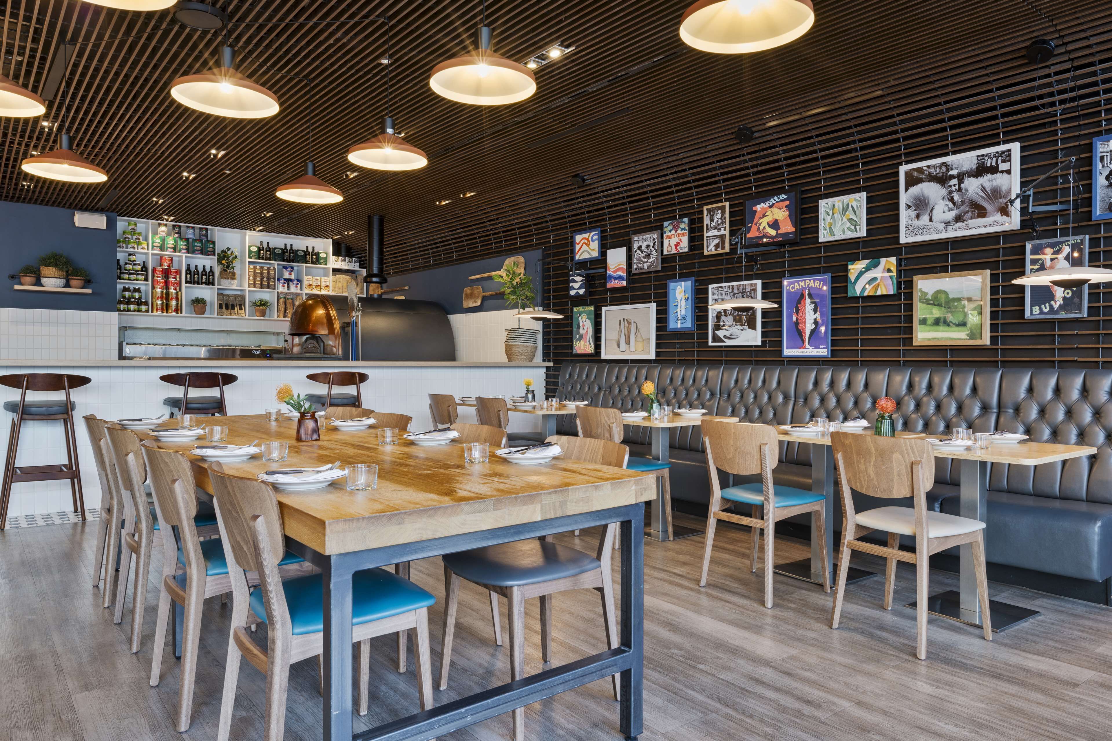 Ein modernes Restaurantambiente mit Holztischen und -stühlen, einer Bar und einer Wand mit gerahmten Kunstwerken.