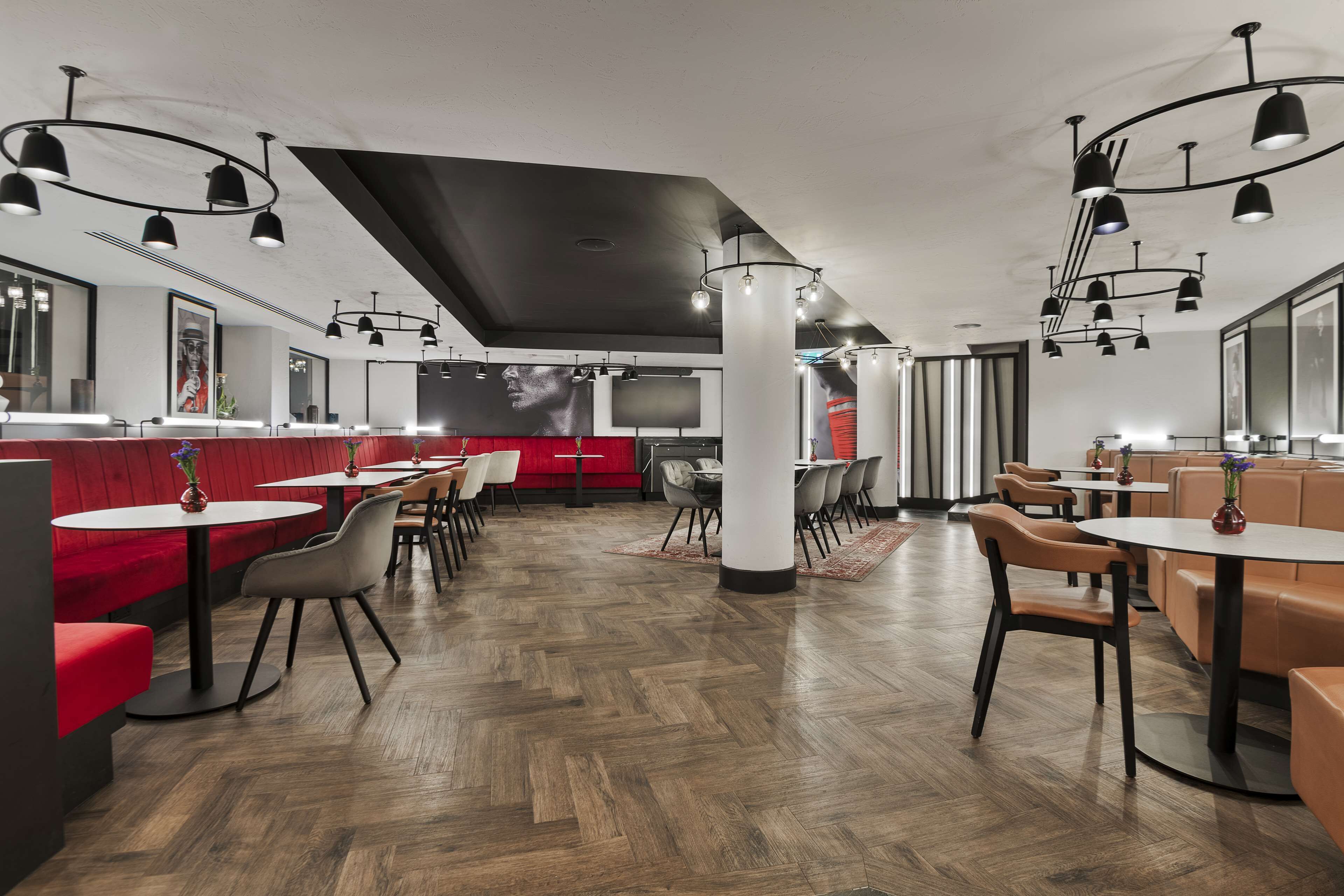 Een modern restaurantinterieur met ronde tafels, beklede zitplaatsen en hanglampen.