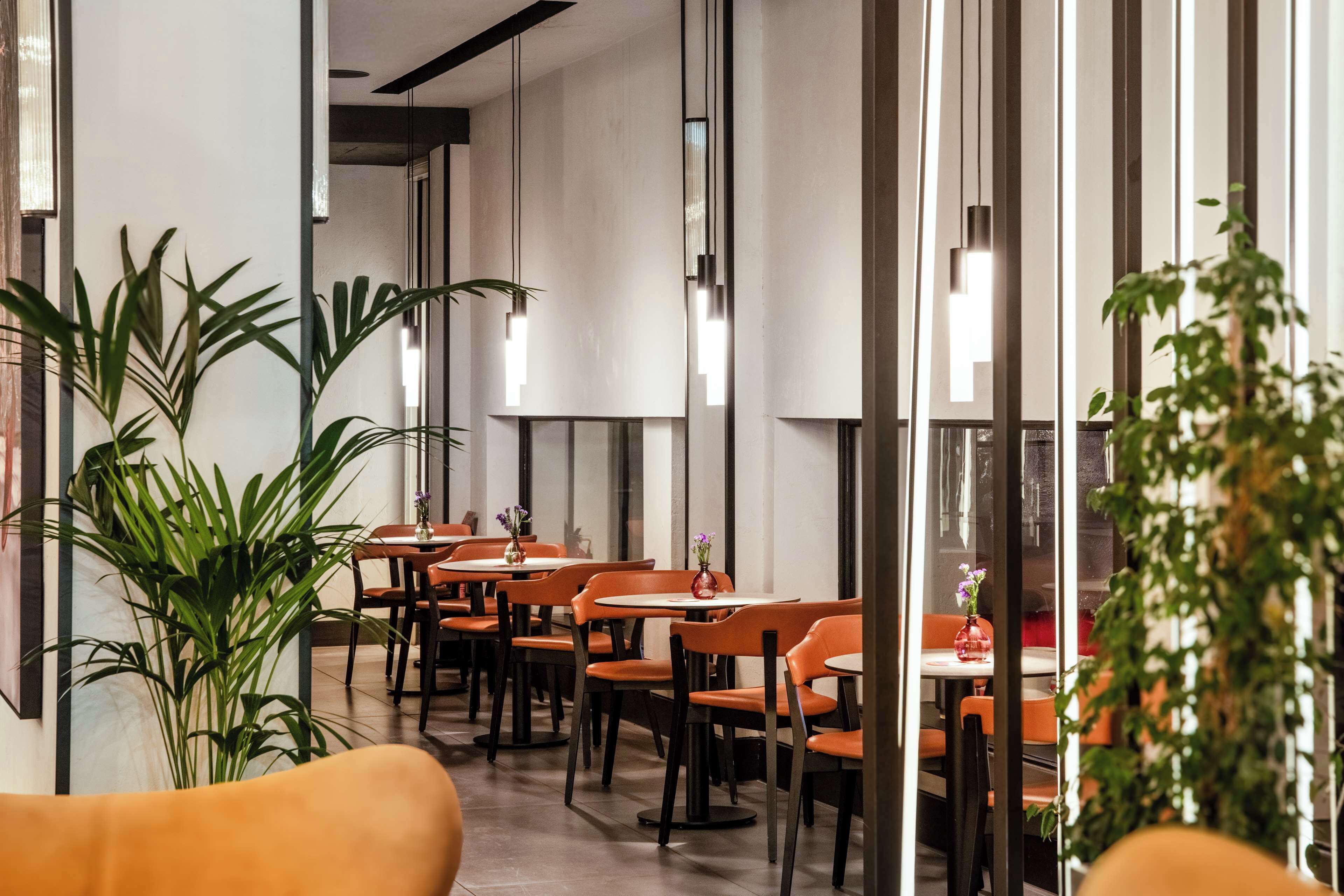 A modern restaurant with high ceilings, pendant lighting, and orange chairs.