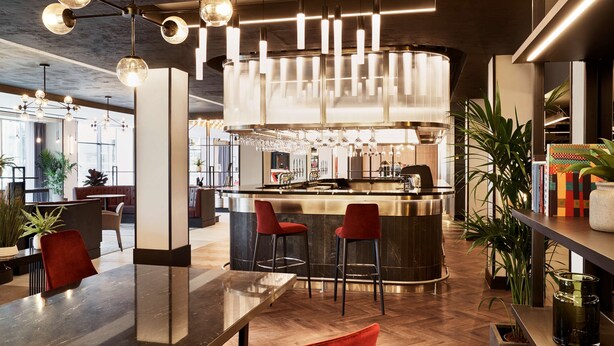 A modern bar area with a central bar, red bar stools, and pendant lighting.