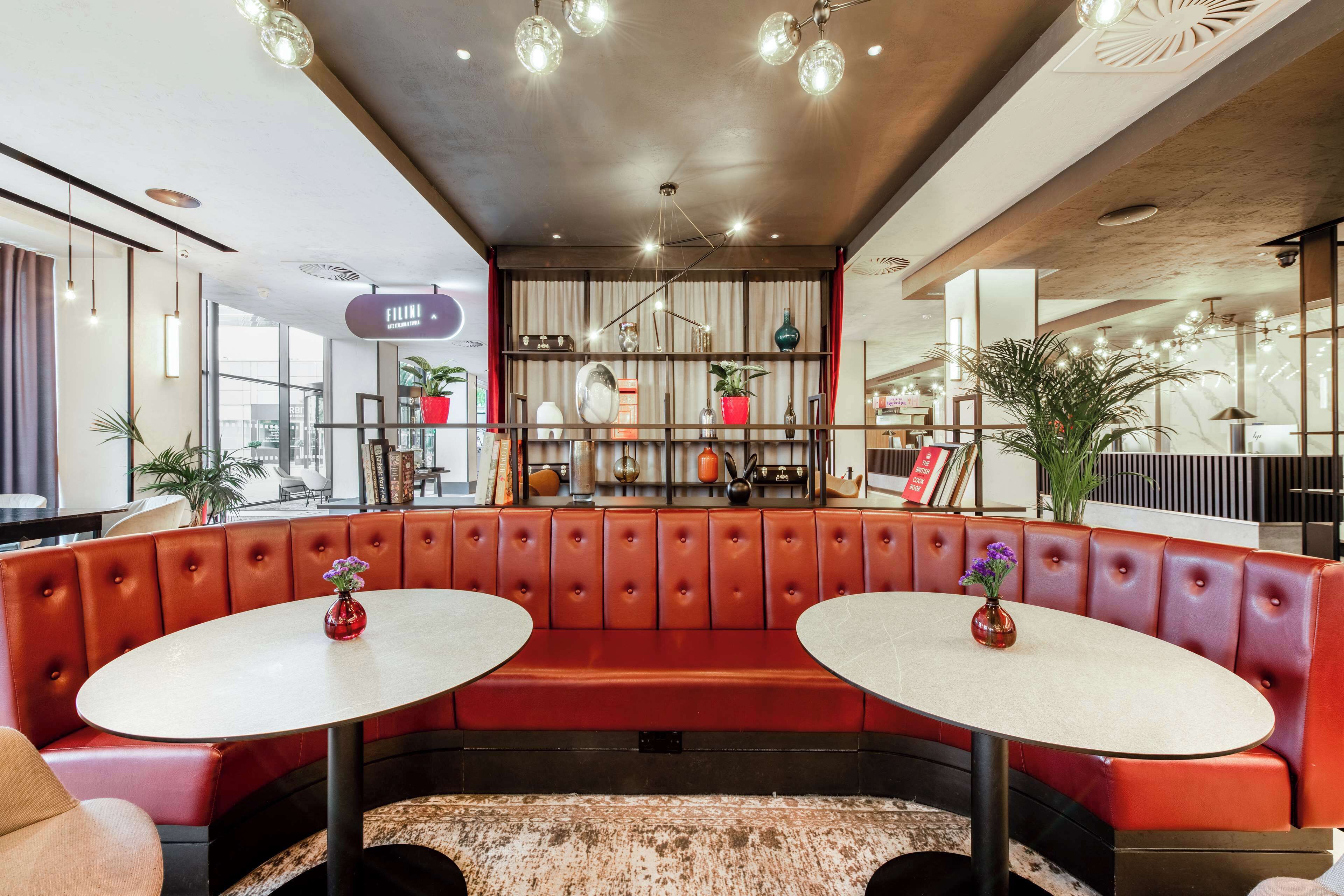 Een modern interieur met een gebogen rode leren zitbank, twee ronde tafels en een decoratieve plank met diverse objecten.
