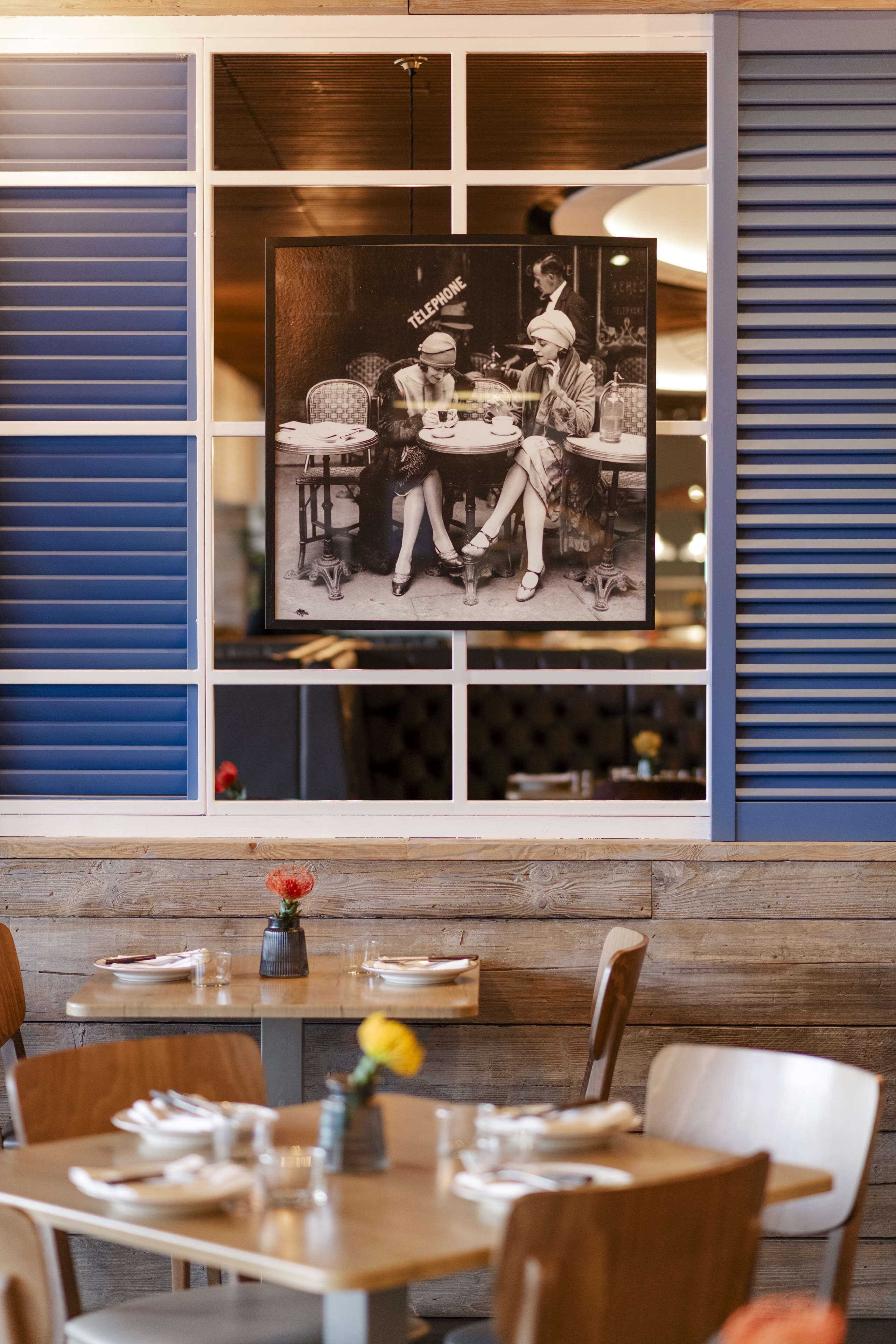 A restaurant interior with a vintage photograph on the wall, wooden paneling, and a table set with plates and glasses.
