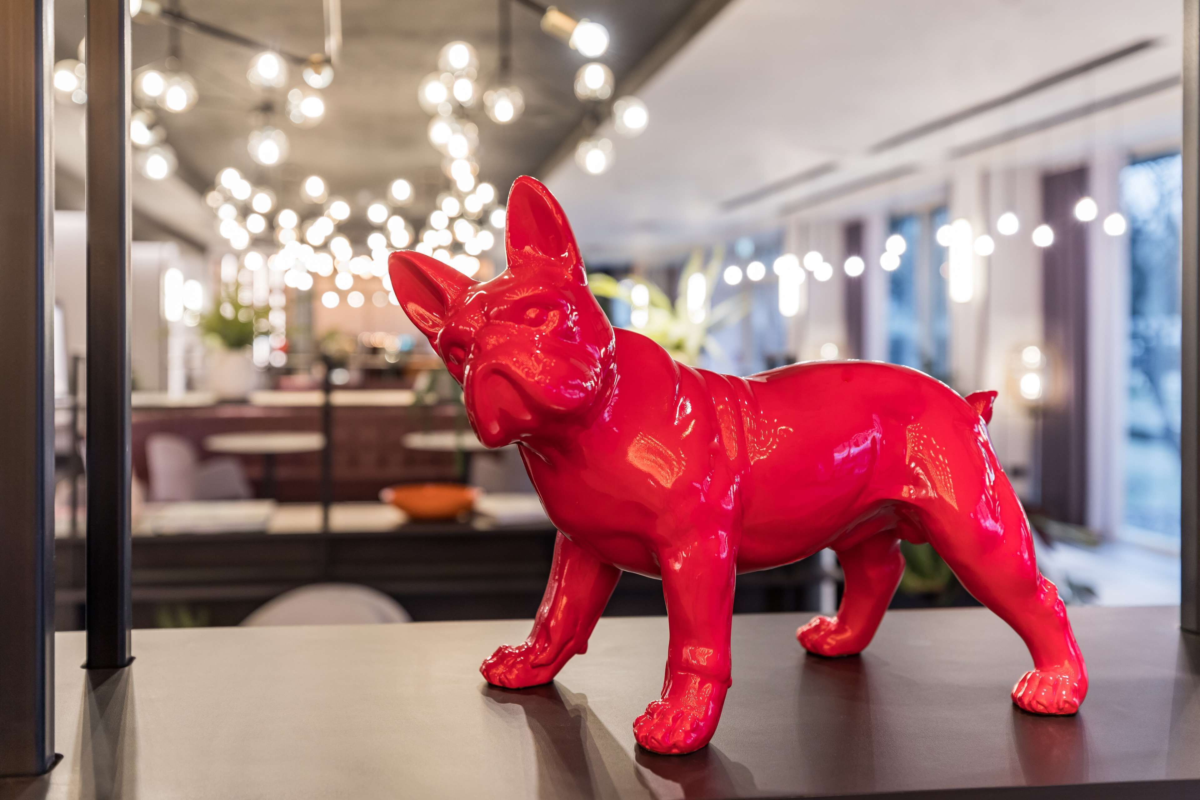 A red dog figurine on a table in a modern interior with hanging lights and a blurred background.