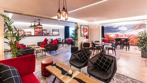 A modern hotel lobby with red and black furniture, a wooden coffee table, and a large painting of wheat on the wall.