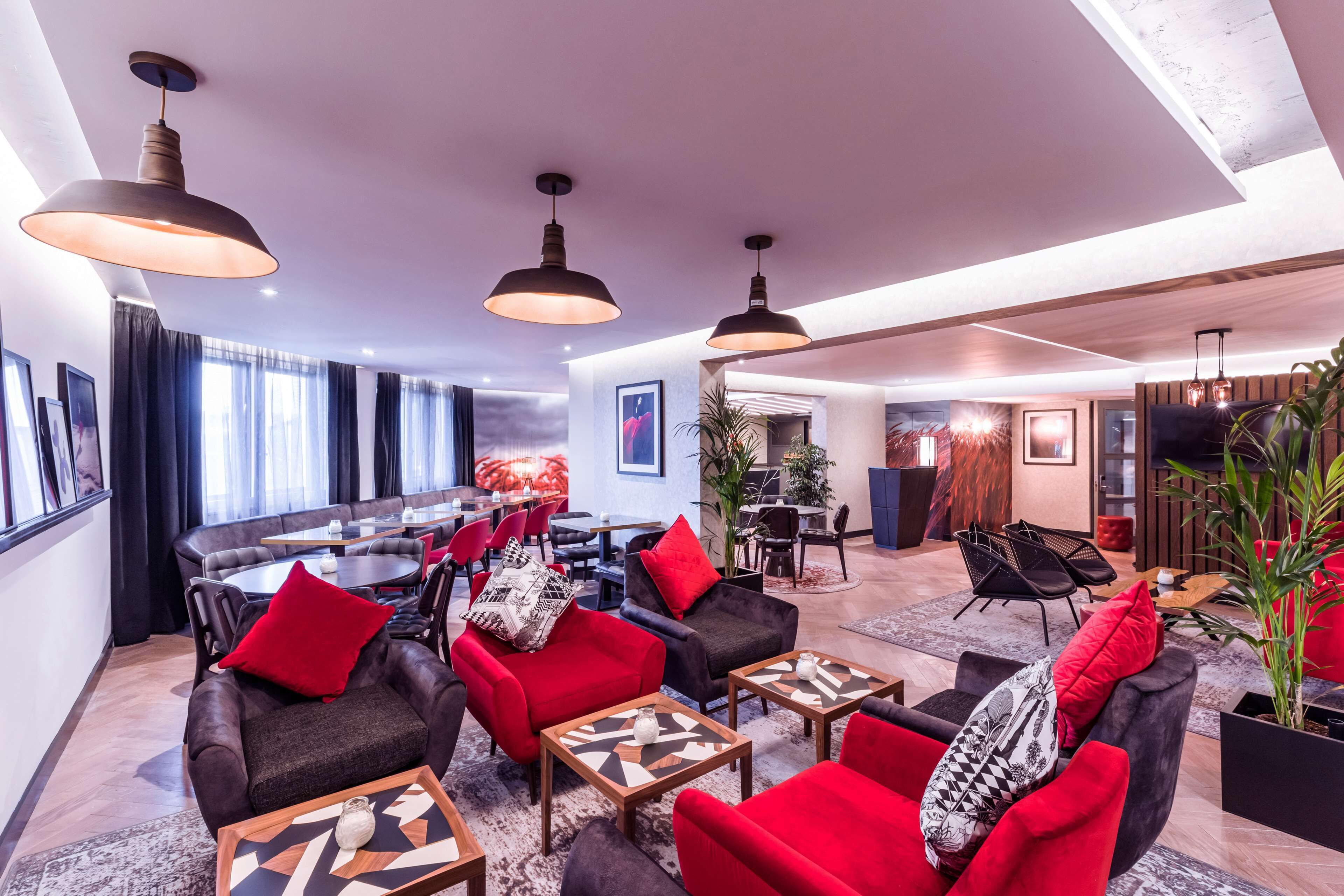 A modern lounge area with leather sofas, red and black armchairs, and a dining area with round tables.