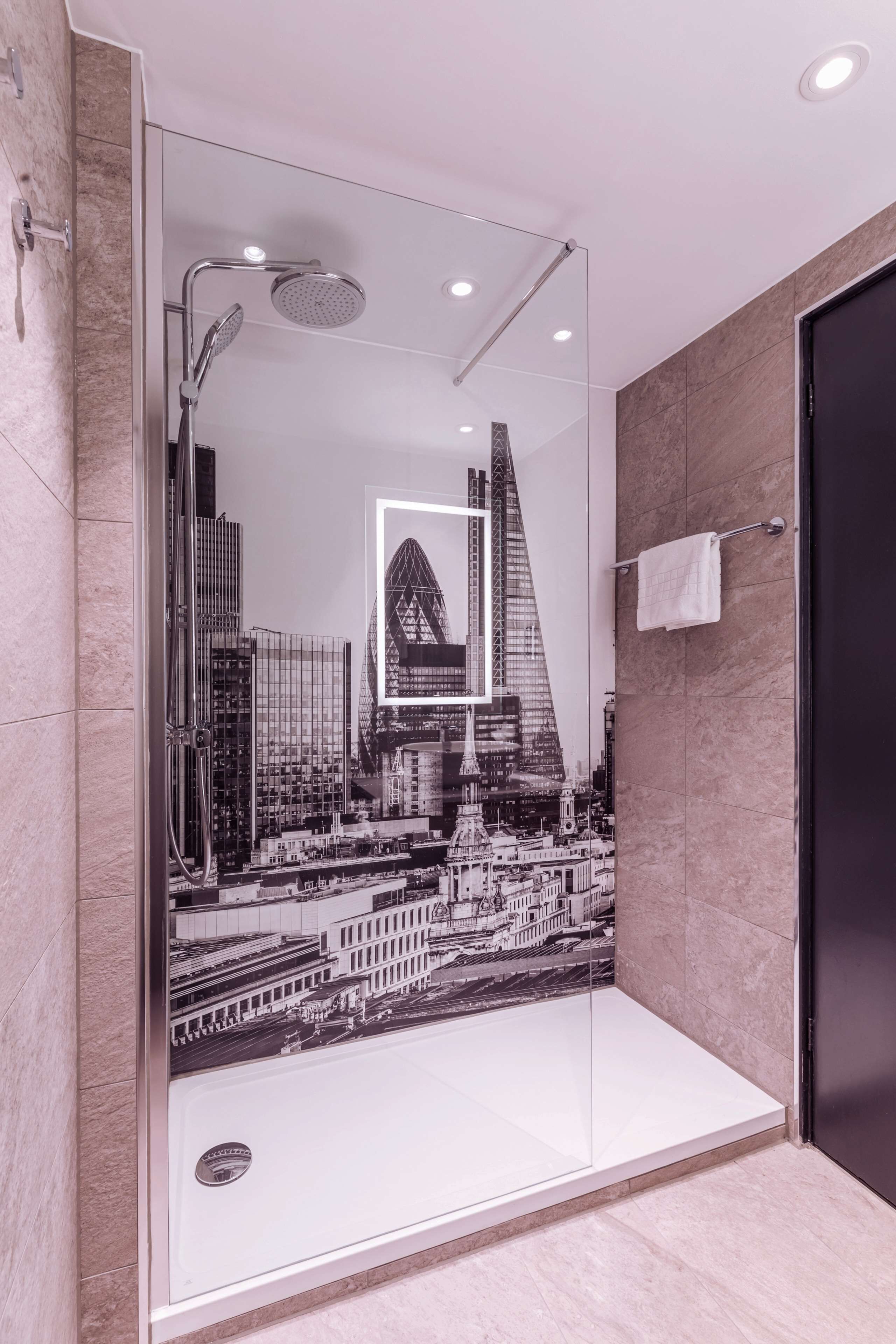 A modern bathroom with a glass shower enclosure, a cityscape mural, and a black door.