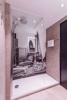 A modern bathroom with a glass shower enclosure, a cityscape mural, and a black door.