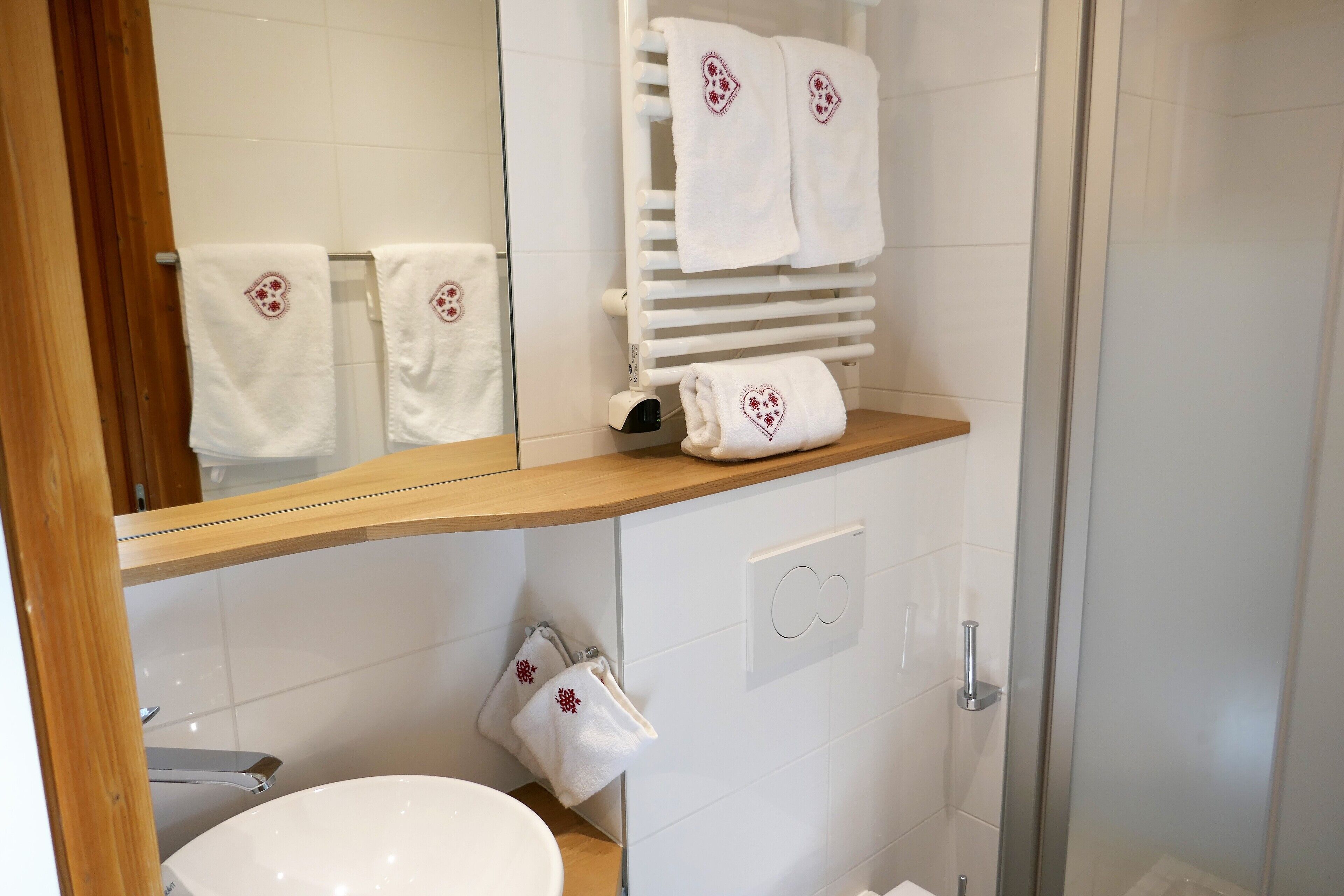 A modern bathroom with a white sink, a mirror, a towel rack with two towels, and a shower area.