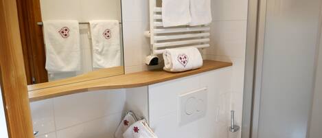 A modern bathroom with a white sink, a mirror, a towel rack with two towels, and a shower area.