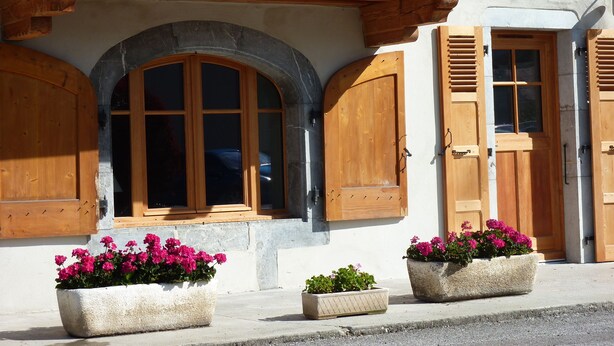Un immeuble doté d’un balcon, de volets en bois et de jardinières.