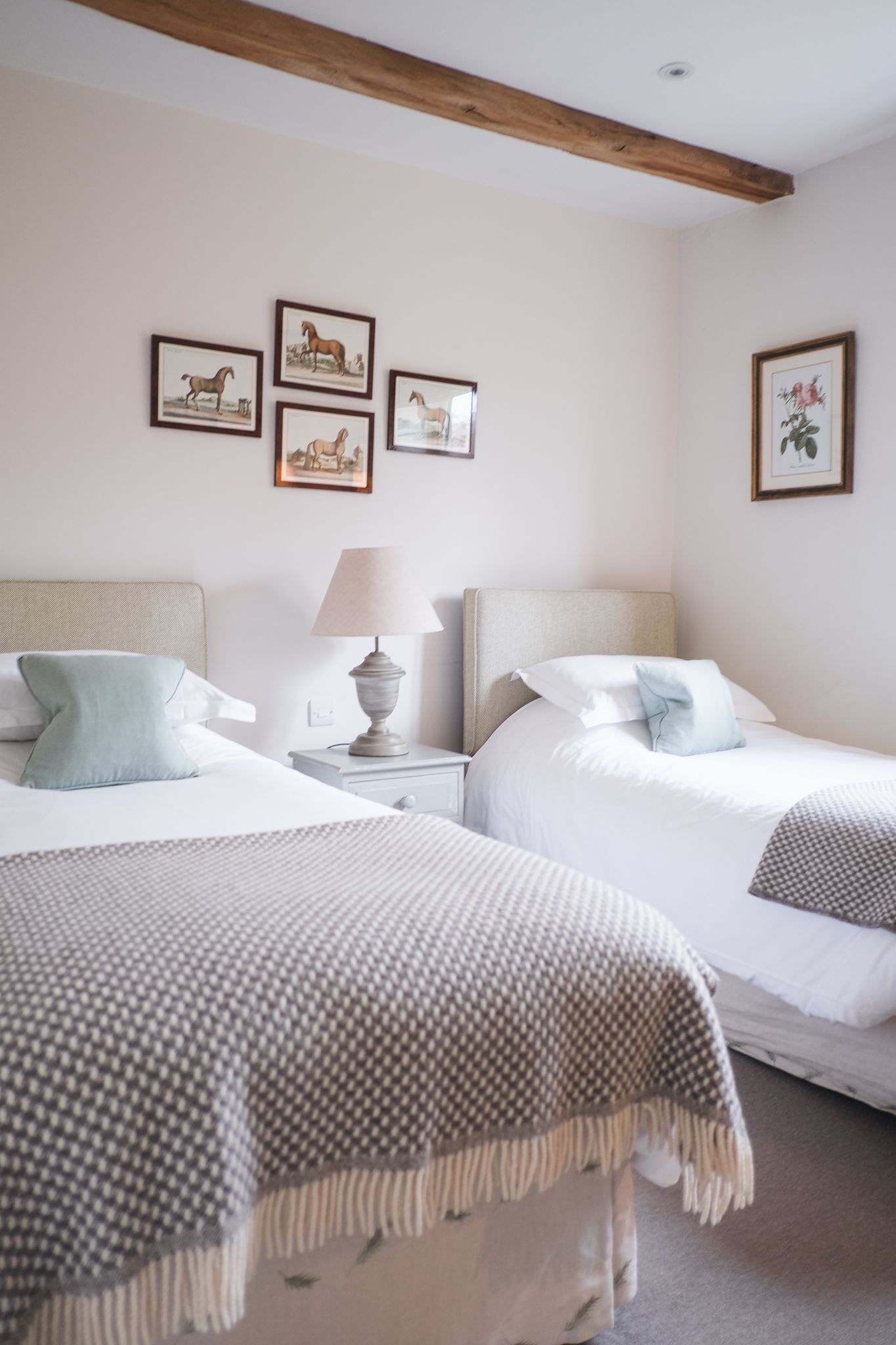 A room with two beds, a nightstand with a lamp, and framed pictures on the wall.
