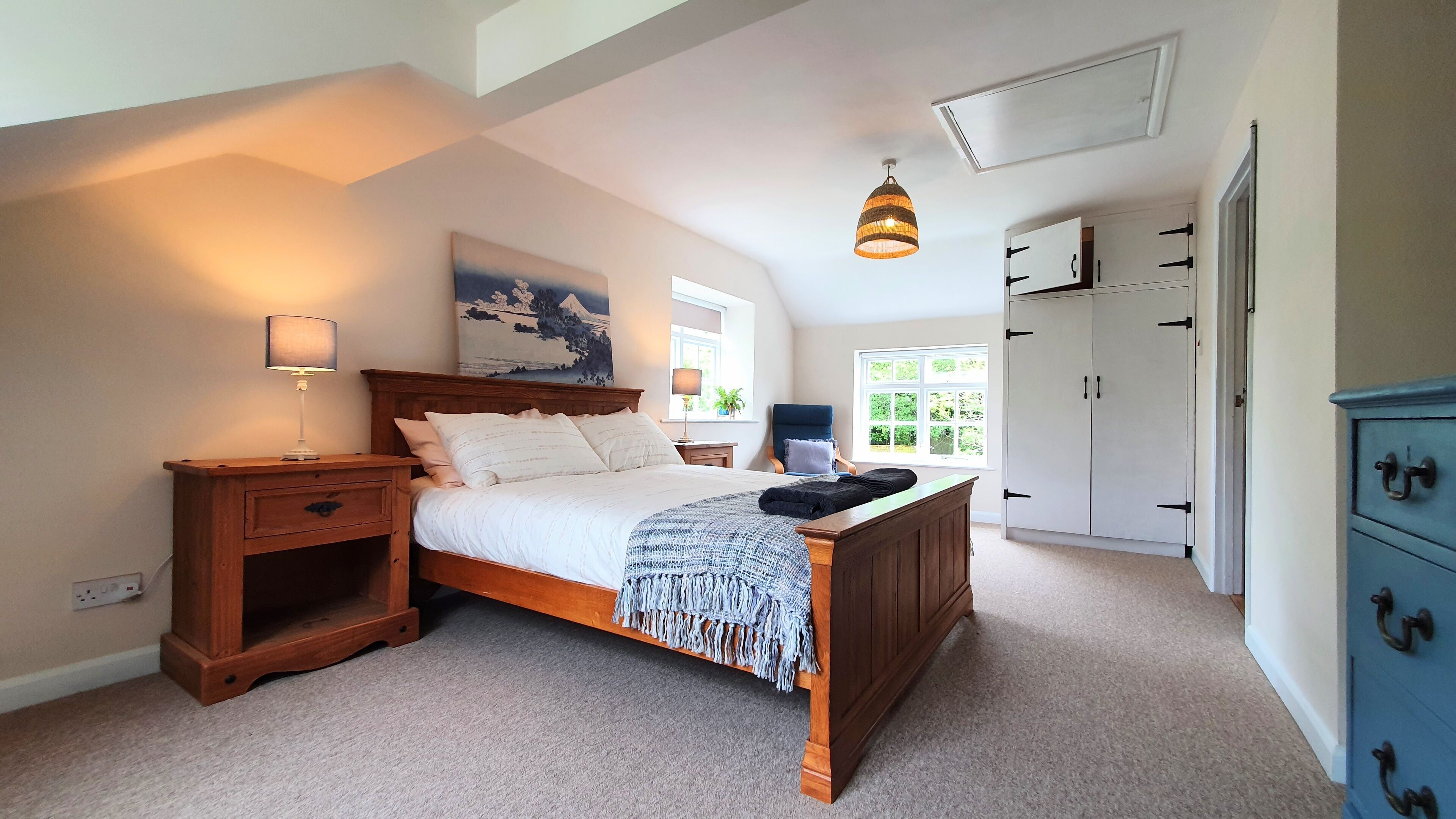 A bedroom with a wooden bed, bedside tables, a lamp, a hanging light, a window, and a wardrobe.