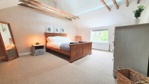 A bedroom with a wooden bed, a nightstand with a lamp, a window with a view, and a radiator. - Beautiful, Quiet, Countryside Cottage in the foothills of the Cotswolds (Witney)