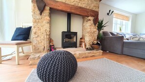 A cozy living room with a stone fireplace, a sofa, a chair, and a knitted pouf. - Beautiful, Quiet, Countryside Cottage in the foothills of the Cotswolds (Witney)