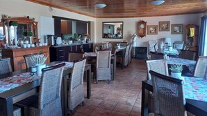 A spacious dining area with multiple tables and wicker chairs, a wooden ceiling, and a kitchen area with cabinets and a mirror. - Acacia Guesthouse (Kathu)