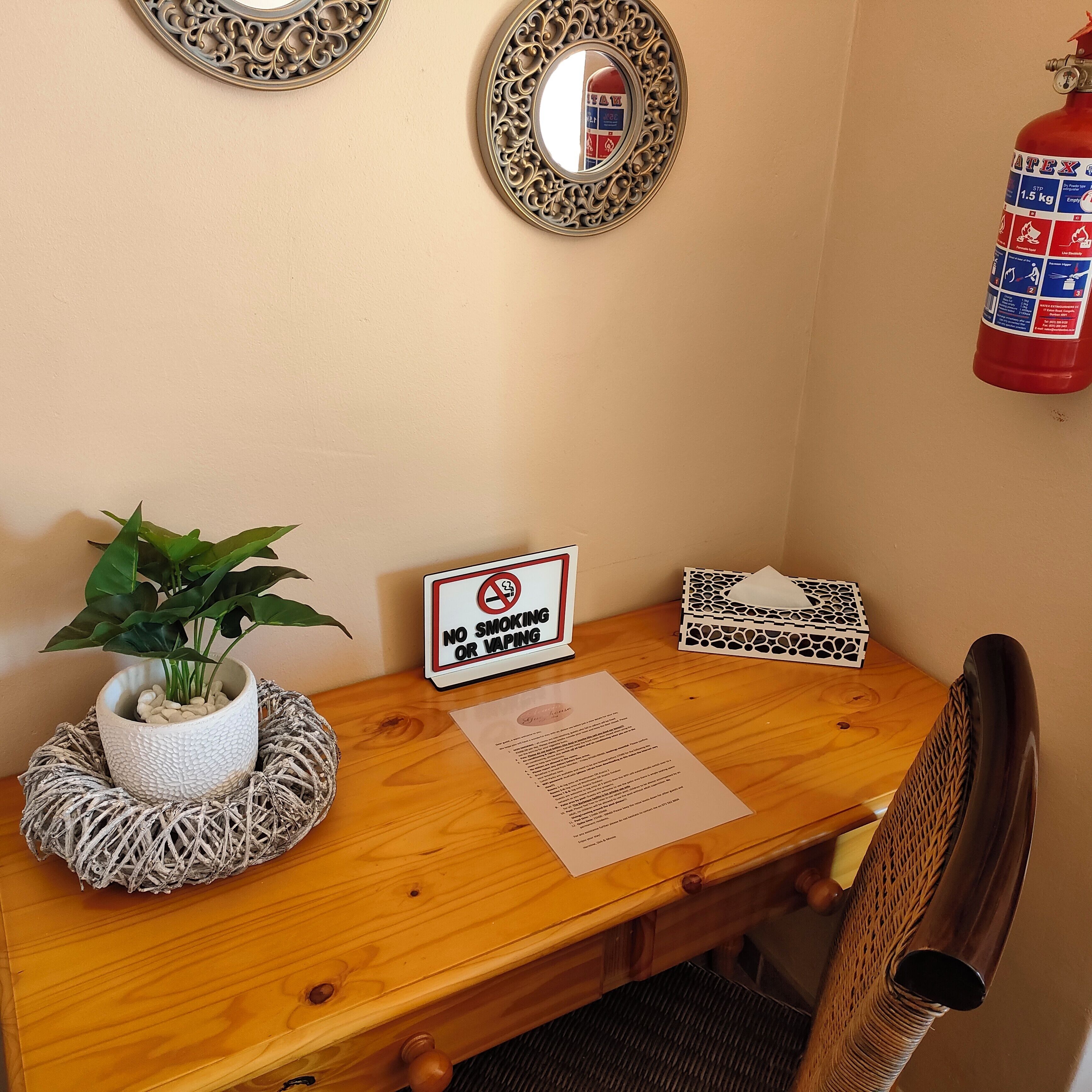 Una mesa de madera con un cartel de prohibido fumar, una planta en maceta, una caja de pañuelos y un extintor de incendios colgado en la pared.