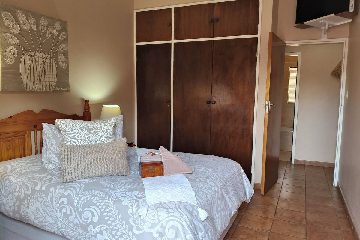 Une chambre à coucher avec un grand lit, une armoire en bois, un téléviseur fixé au mur et un tableau accroché au mur.