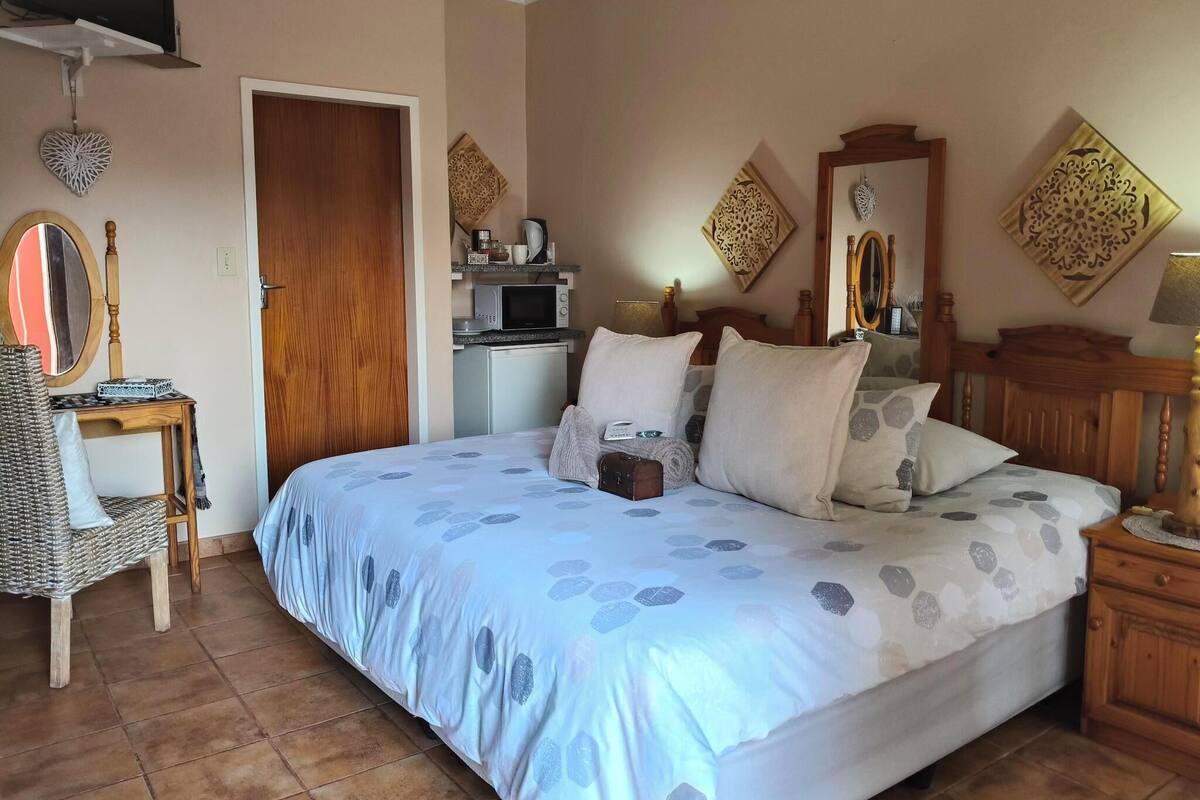 Une chambre avec un grand lit, une commode en bois, un petit bureau avec une chaise, un four à micro-ondes et un téléviseur posé sur une étagère.