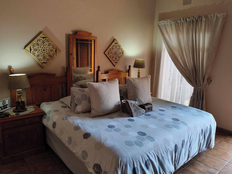 Quarto com cama, cabeceira de madeira, almofadas estampadas, mesa de cabeceira com abajur e janela com cortinas.