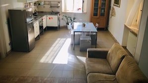 Une cuisine compacte équipée d’un réfrigérateur, d’une cuisinière, d’un évier et de placards. On y trouve une table à manger avec des chaises, ainsi qu’un canapé dans l’espace salon.
