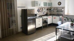 Une cuisine moderne équipée d’un réfrigérateur en acier inoxydable, d’une cuisinière à gaz et d’un four à micro-ondes. On y trouve une table à manger avec des chaises et une plante en pot.