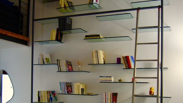 Une pièce avec une grande bibliothèque étroite remplie de livres, une échelle, un bureau avec un ordinateur et un téléviseur.