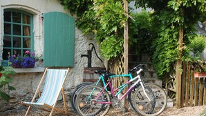 Een fiets geparkeerd naast een gestreepte stoel en een stenen muur met een raam en groene luiken.