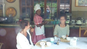 Una cocina con mostrador, microondas y cafetera. Tres personas sentadas en una mesa con tazas y tetera.