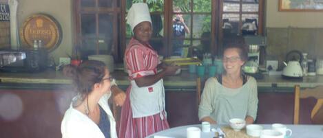 Una cocina con mostrador, microondas y cafetera. Tres personas sentadas en una mesa con tazas y tetera.