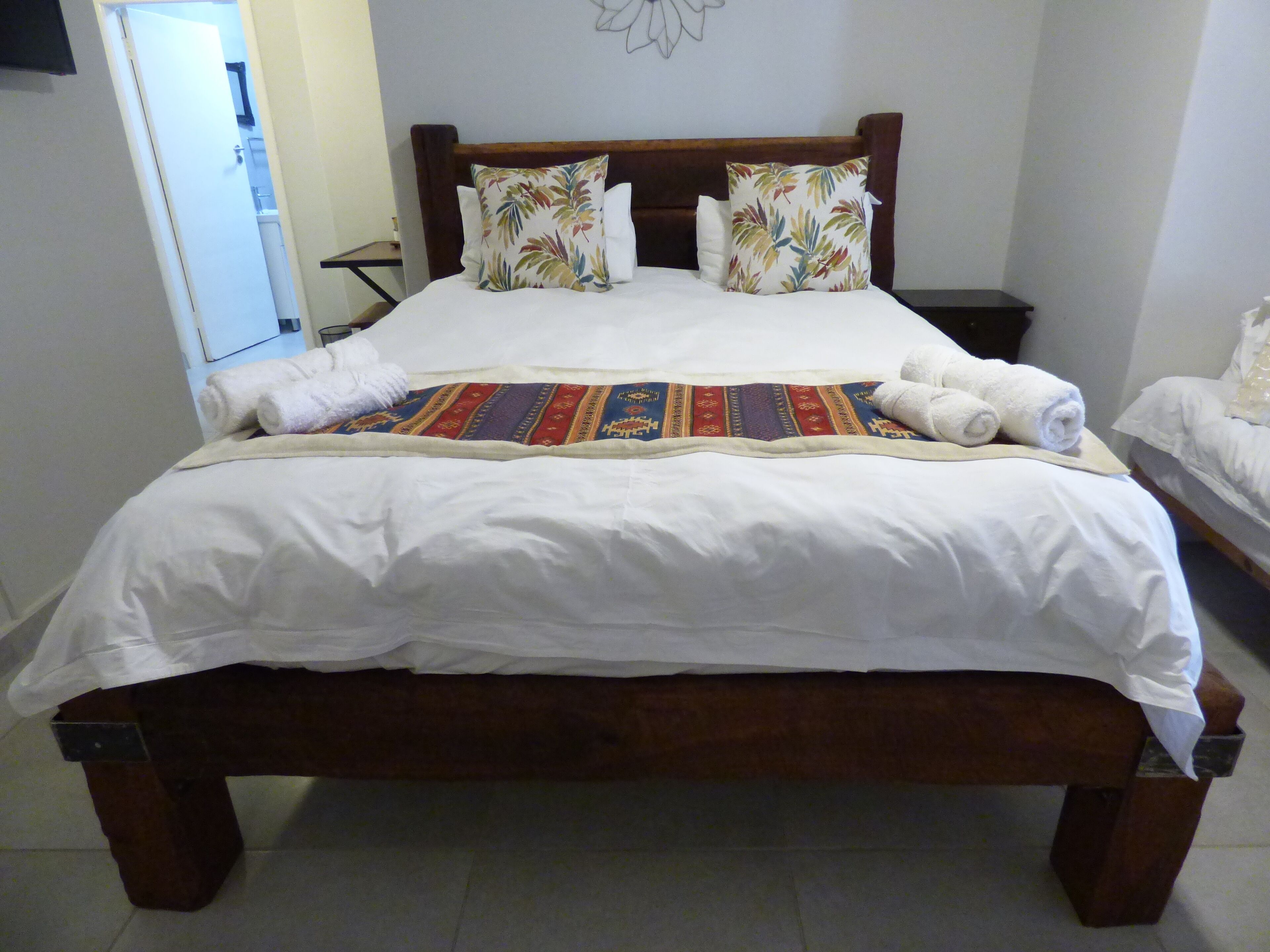 Un lit bien fait, avec des draps blancs, une couvre-lit colorée et deux coussins décoratifs.