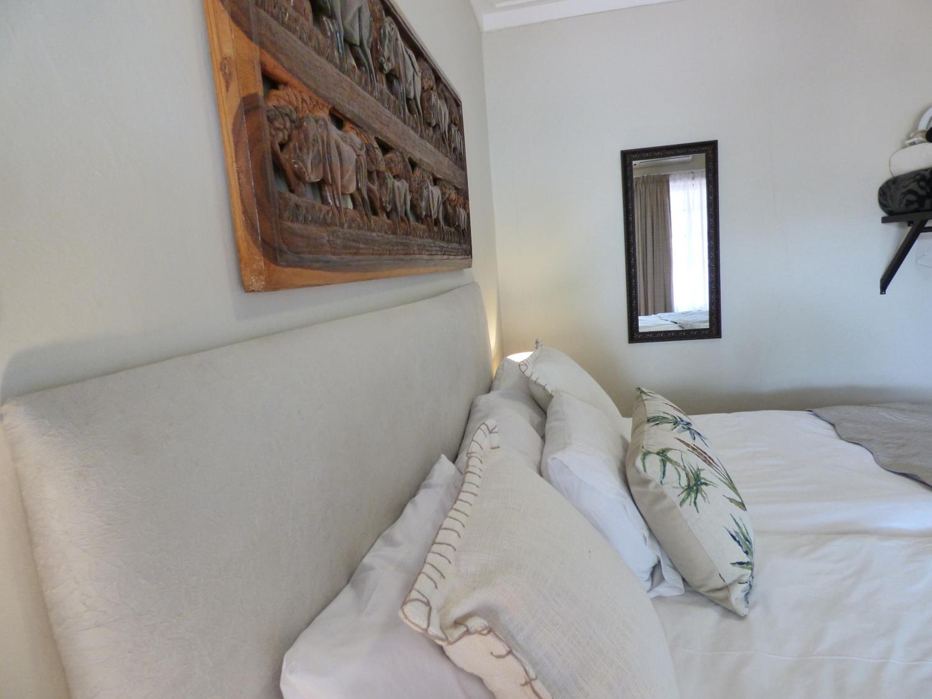 Een slaapkamer met een bed, kussens, een houten wanddecoratie en een spiegel.