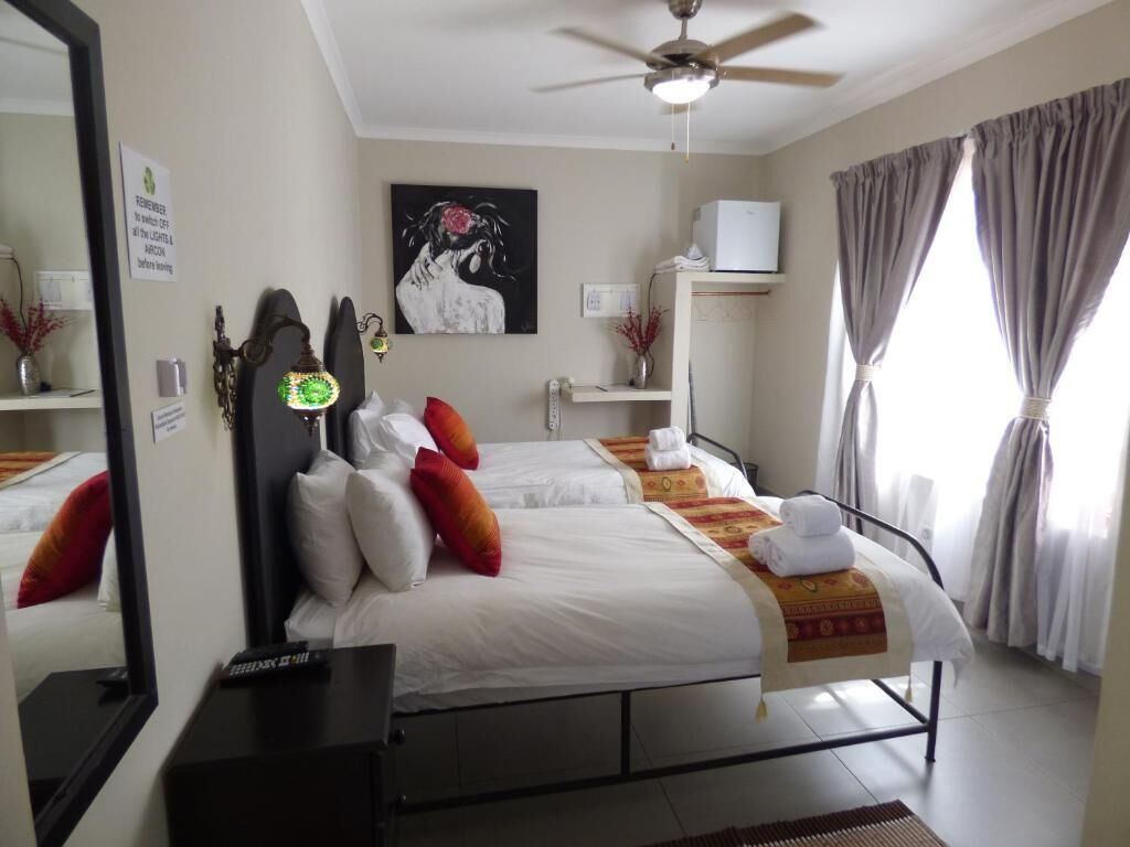 Une chambre d’hôtel avec deux lits, un ventilateur de plafond, un tableau au mur et une fenêtre avec des rideaux.