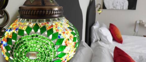 Una habitación con cama, almohadas, un cuadro en la pared y una lámpara decorativa con diseño de mosaico.