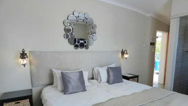 Una cama bien hecha con un espejo grande encima, dos apliques de pared y una cesta sobre una mesita de noche.