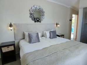 A neatly made bed with a large mirror above it, two wall sconces, and a basket on a nightstand.