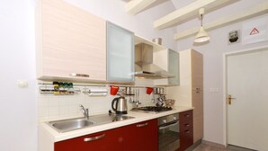A compact kitchen with a sink, stove, and oven, featuring red cabinets and white countertops.