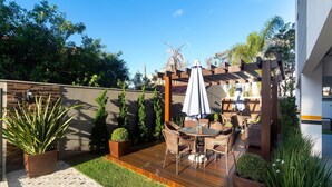 A patio with a wooden deck, outdoor furniture, and a pergola with a white umbrella. - Aluguel Apartamento 2 quartos sendo 1 suíte - 522 (Bombinhas)