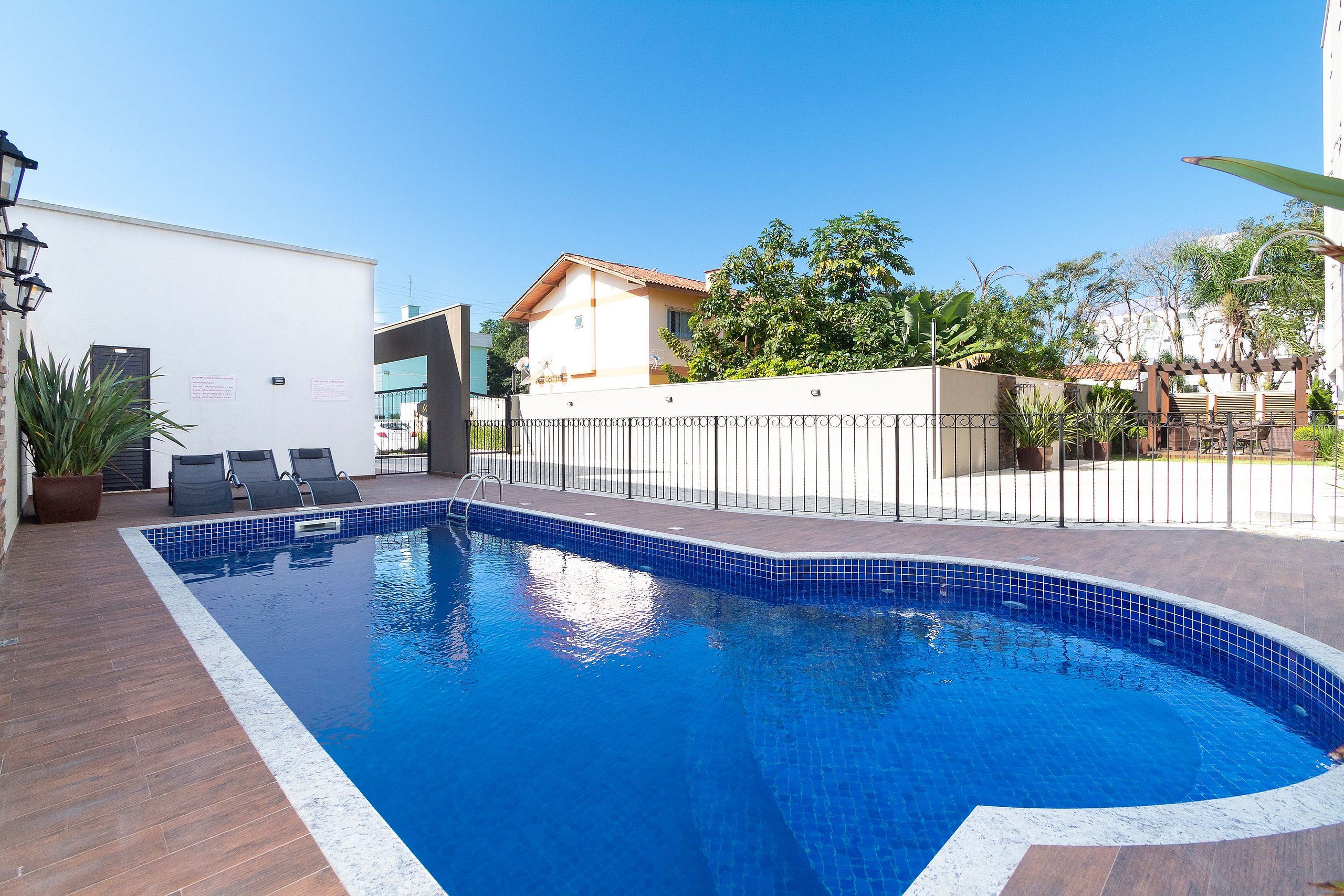 Una piscina con borde de azulejos, rodeada por un muelle de madera y una valla de metal.