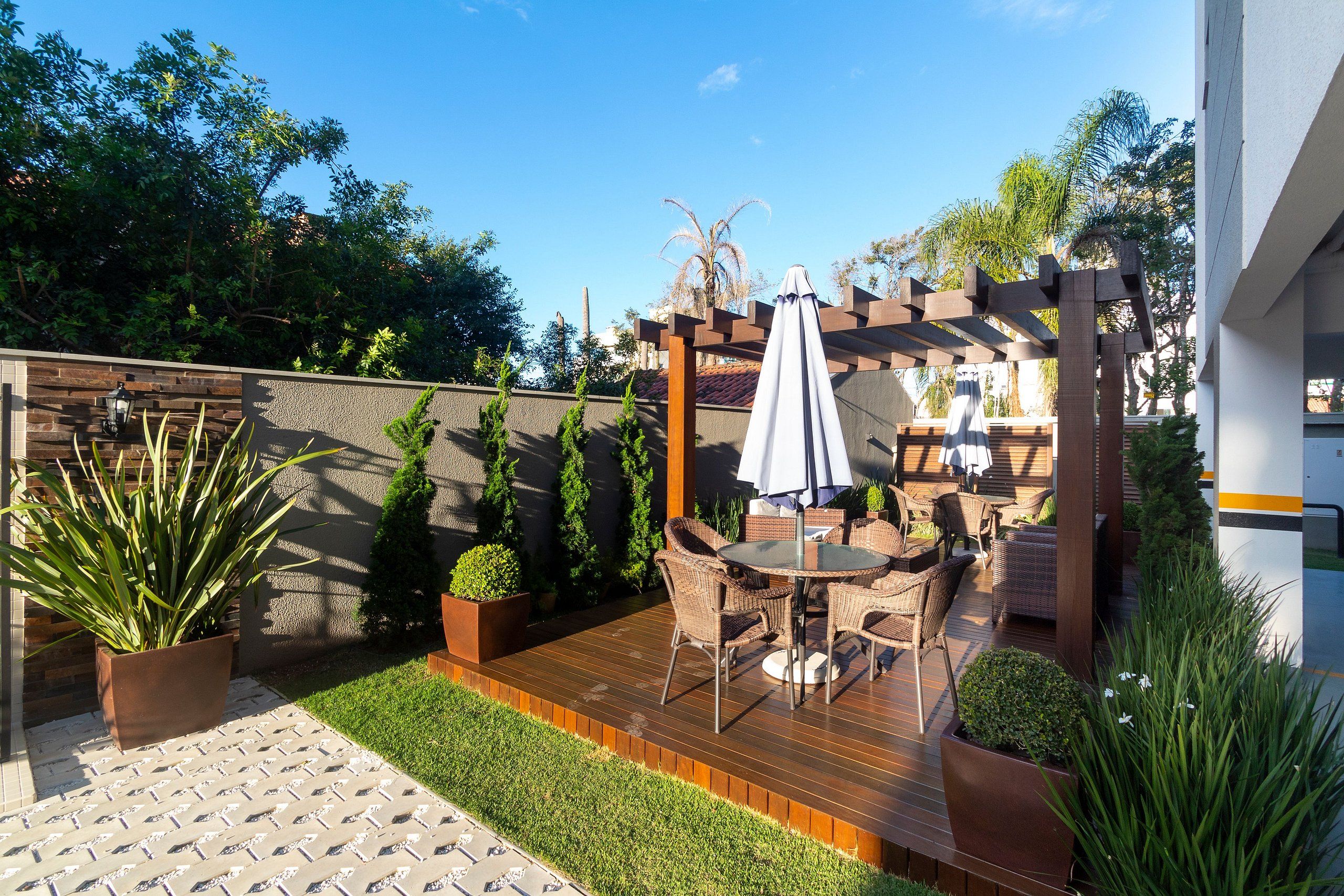 A patio with a wooden deck, outdoor furniture, and a pergola with a white umbrella.