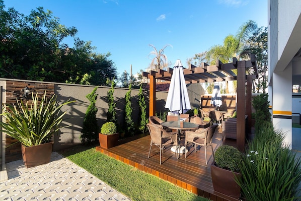 A patio with a wooden deck, outdoor furniture, and a pergola with a white umbrella. - Aluguel Apartamento 2 quartos sendo 1 suíte - 522 (Bombinhas)