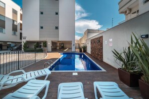 A swimming pool with lounge chairs, a brick wall, and a building in the background. - Aluguel Apartamento 2 quartos sendo 1 suíte - 522 (Bombinhas)