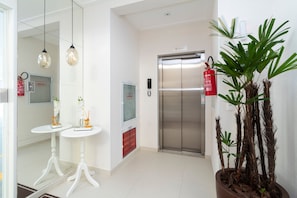 A clean, modern lobby with a reception desk, a fire extinguisher, an elevator, and a potted plant. - Aluguel Apartamento 2 quartos sendo 1 suíte - 522 (Bombinhas)