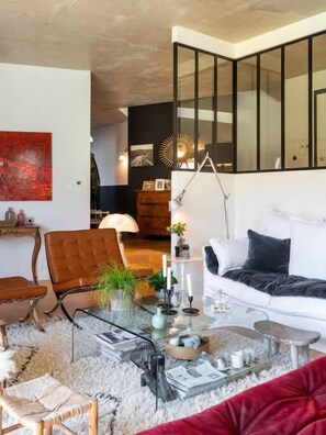 A modern living room with a white sofa, a glass coffee table, and a red chair. There is a large mirror on the wall and a lamp on a side table. - Togo - Stunning contemporary architect's house (Tassin-la-Demi-Lune)